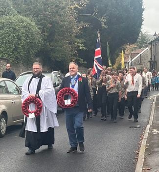Image shows the Rev'd Nigel and SPC Chair Cllr Jon Godfrey as part of the parade from the Church to the War Memorial, with members of 1st Saltford Scouts behind. Image taken on High Street, Remembrance Sunday 2025